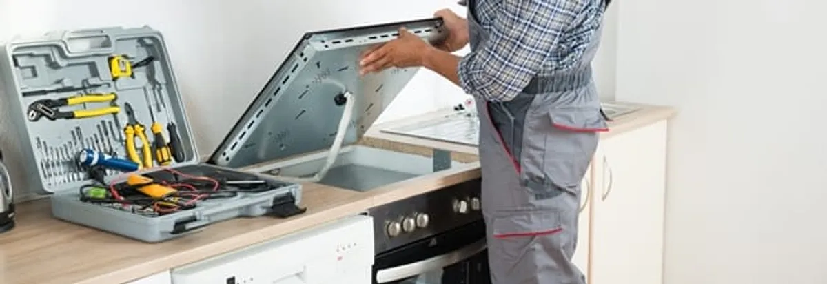 Cooktop repair technician lifting a built-in stovetop for service in New Haven, CT