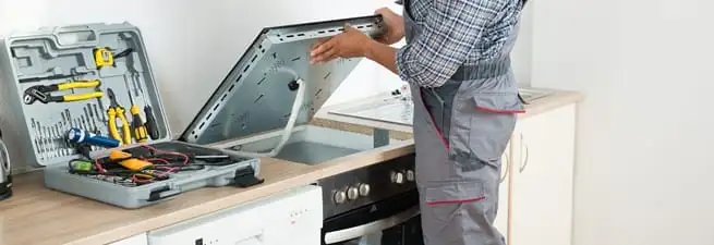 Cooktop repair technician lifting a built-in stovetop for service in New Haven, CT
