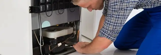 Refrigerator repair technician servicing the compressor and condenser area in New Haven, CT