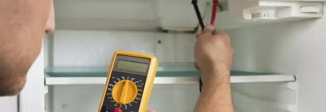 Refrigerator repair technician testing electrical components with a multimeter in New Haven, CT
