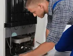 Refrigerator repair technician servicing the compressor and condenser area in New Haven, CT